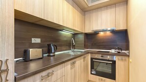 A compact kitchen with wooden cabinets, a built-in oven, a coffee maker, and a toaster. - Apartments in Golden Sands (Varna)