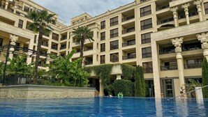 A multi-story hotel with a swimming pool, palm trees, and ornate architectural details. - Apartments in Golden Sands (Varna)