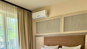 Et hotelværelse med en stor seng, et træhovedgærde, en balkon med gardiner og en aircondition.