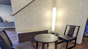 Un interior moderno con una mesa redonda y dos sillas, una escalera y una lámpara fijada a la pared.