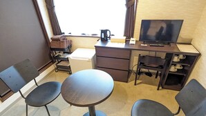Habitación de hotel con escritorio, dos sillas, televisor, cafetera y ventana con cortinas.