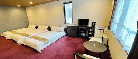 Ein Hotelzimmer mit zwei Betten, einem Schreibtisch mit Computer, einem Sessel, einem kleinen Tisch und einem Fenster mit Vorhängen.