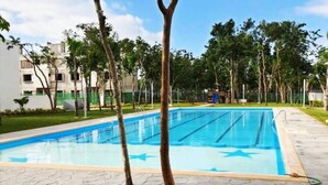 Piscina com pistas demarcadas, rodeada por árvores e um calçadão.