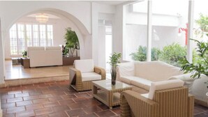 Uma sala de estar ampla com sofá branco, mobiliário de vime e uma mesa de centro de vidro.