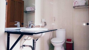 Un baño con un lavabo, dos llaves, un inodoro y un cubo de basura.