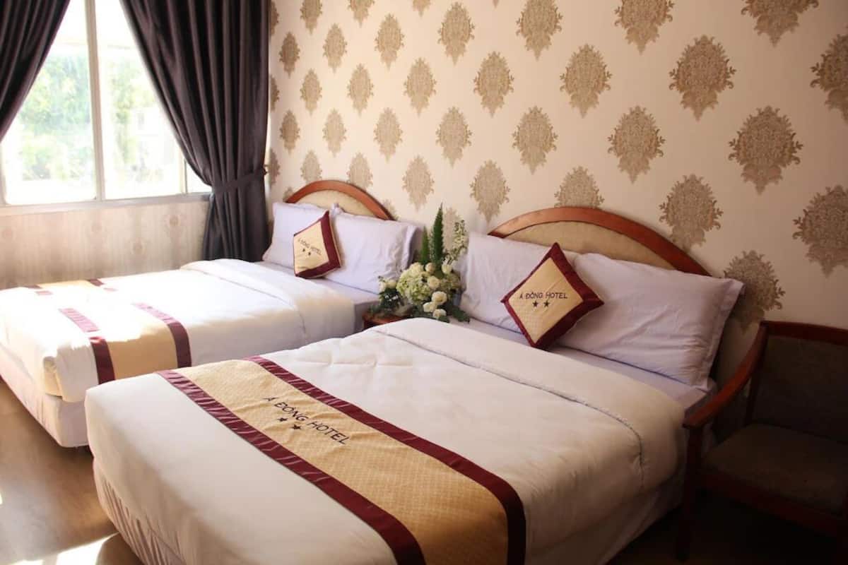 Une chambre d’hôtel avec deux lits, chacun doté d’une tête de lit, d’un arrangement floral et d’une couvre-lit portant le nom de l’hôtel.