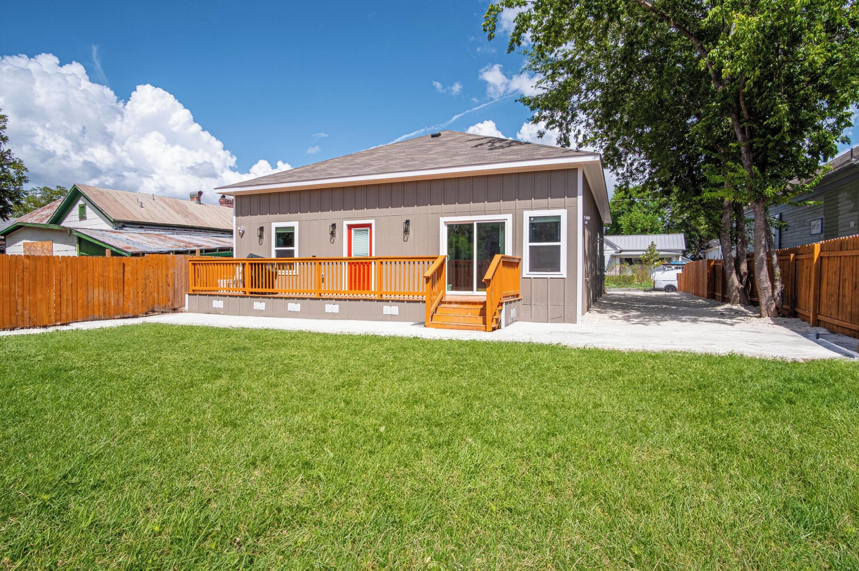 A single-story house with a front deck, a red door, and a small front yard.
