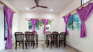 Un comedor con una mesa redonda y seis sillas, cortinas moradas y un ventilador de techo.