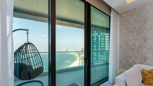 Ein modernes Wohnzimmer mit Glastür, die auf einen Balkon mit Blick auf Strand und Stadtbild führt.