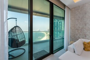 A modern living room with a glass door leading to a balcony overlooking a beach and cityscape.