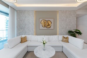 Un salon moderne avec un canapé d’angle blanc, une table basse en marbre et un grand tableau abstrait accroché au mur.