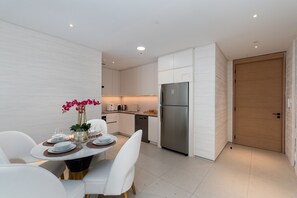 Een moderne keuken met witte kasten, een roestvrijstalen koelkast, en een eethoek met witte stoelen en een tafel gedekt voor twee personen.