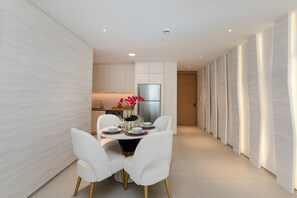 Une cuisine moderne avec des meubles blancs, un réfrigérateur en acier inoxydable et un coin repas comprenant des chaises blanches et une table ronde.