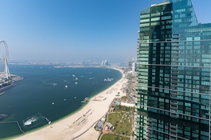 Een kustgezicht met een modern hoog gebouw, een strand en een groot reuzenrad in de verte.