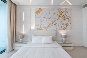 A modern bedroom with a large bed, two bedside tables with lamps, a marble wall art piece, and a large window with curtains.