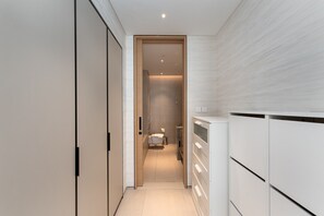Un couloir étroit, avec un lit au fond, une armoire à gauche et un meuble blanc à droite.