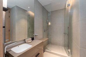 Een moderne badkamer met een douche met glazen wand, een beige wastafelmeubel met een wastafel en een grote spiegel.