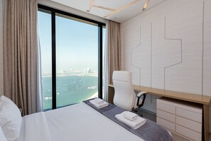 A modern hotel room with a large bed, a desk, and a view of a cityscape and water.