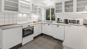 Una cocina moderna con armarios blancos, horno empotrado, microondas y un ventanal que proporciona luz natural.