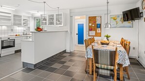 Una cocina moderna con armarios blancos, un comedor con una mesa redonda y sillas, y una puerta azul que da a otra habitación.