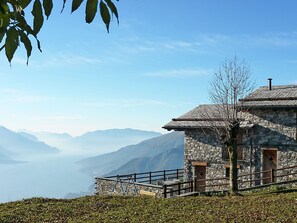 Um edifício de pedra com guarda-corpo metálico, céu limpo e montanhas ao fundo.