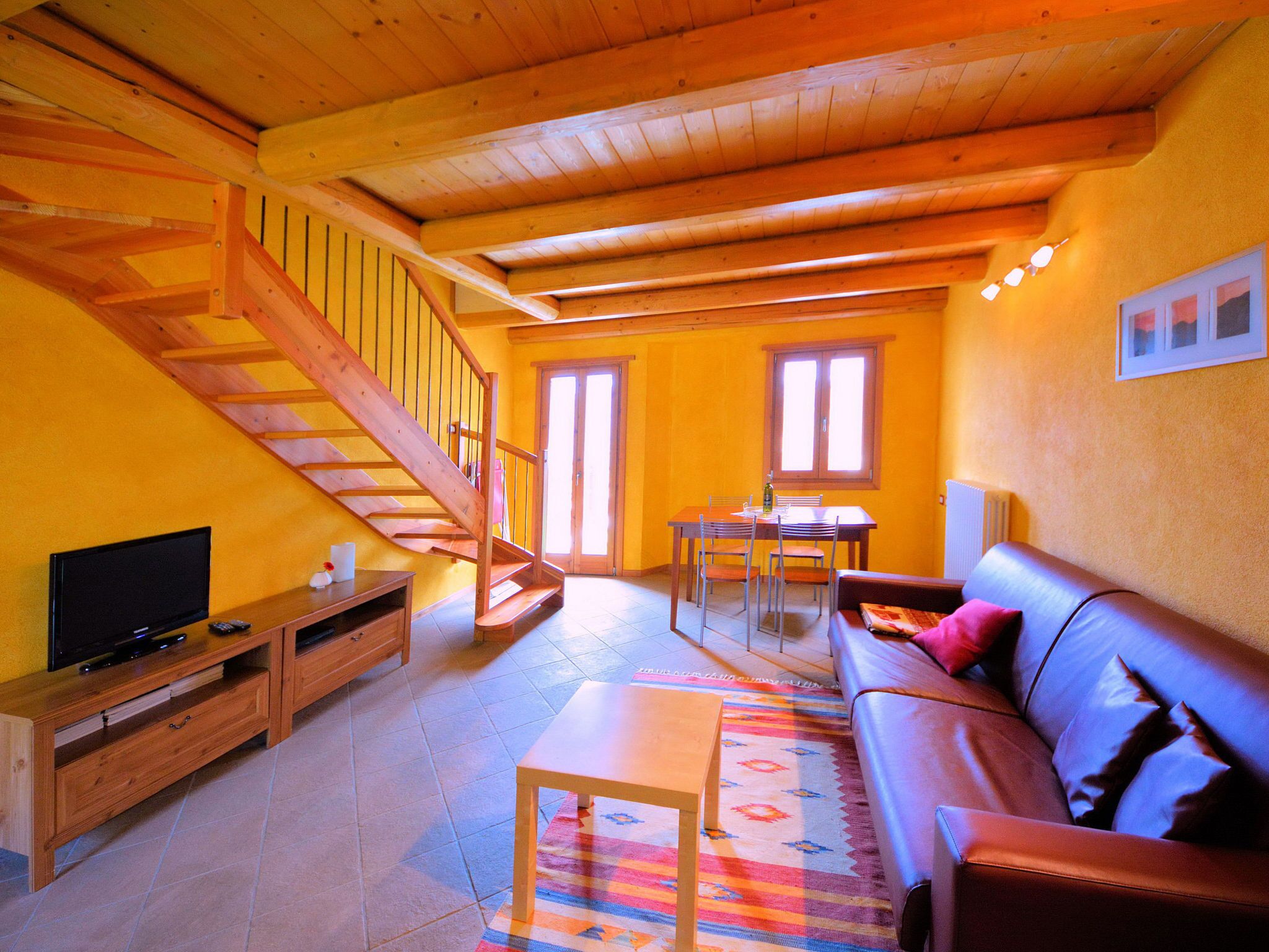 A cozy living room with a wooden staircase, a sofa, a TV, and a dining area.