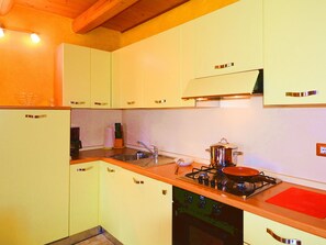 Une cuisine avec des meubles blancs, un évier, une cuisinière et une planche à découper rouge.