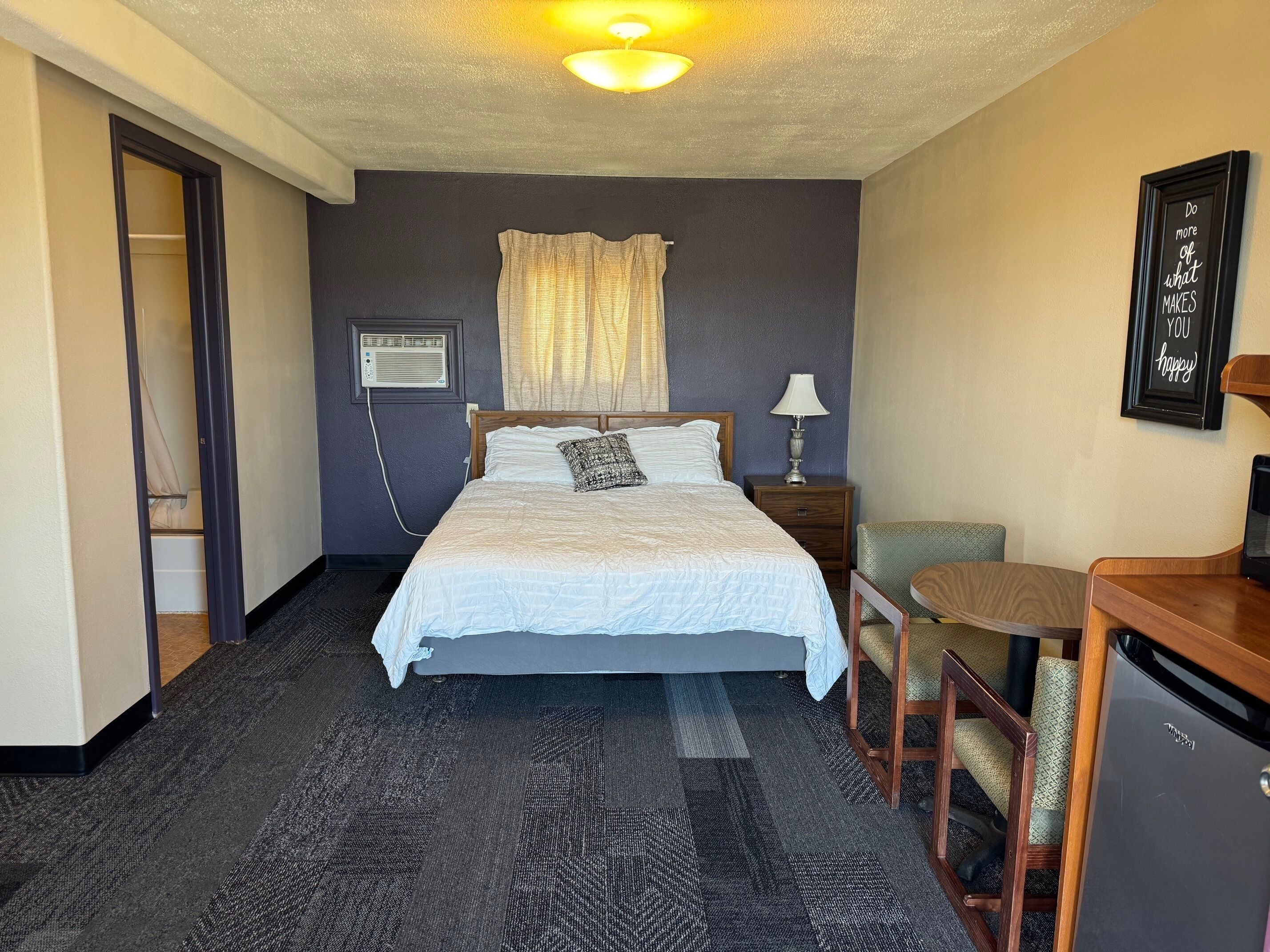 A hotel room with a bed, bedside table, lamp, chair, and a desk with a computer.