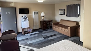 A compact living room with a sofa, a small table, a TV, and a kitchenette area.