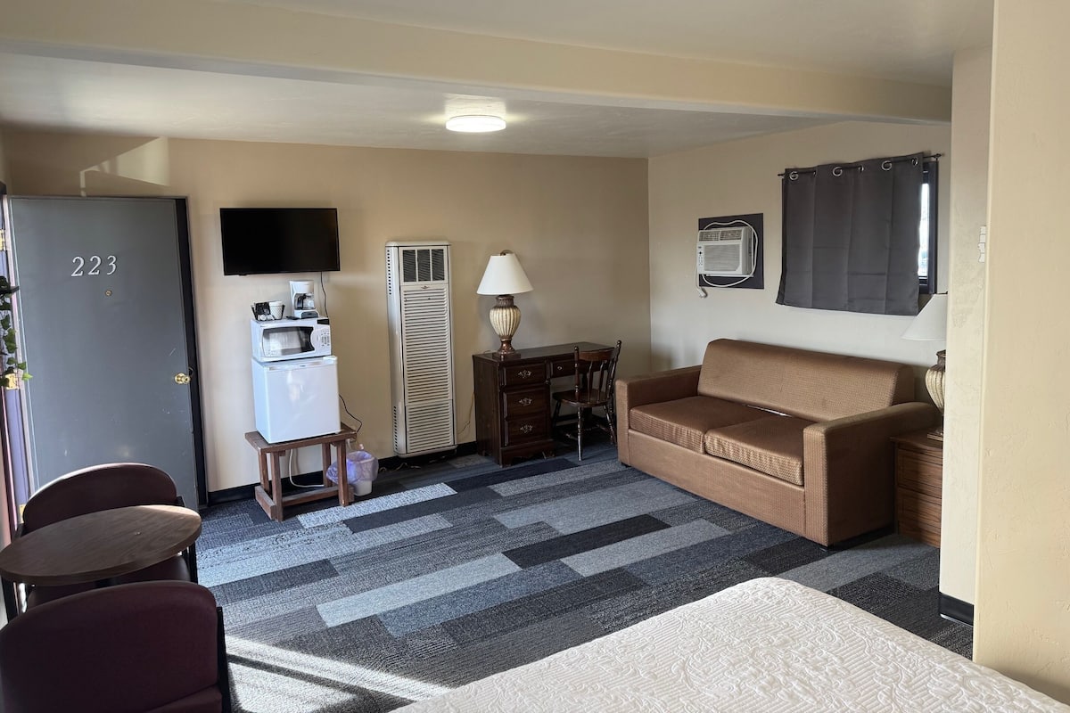 A compact living room with a sofa, a small table, a TV, and a kitchenette area.