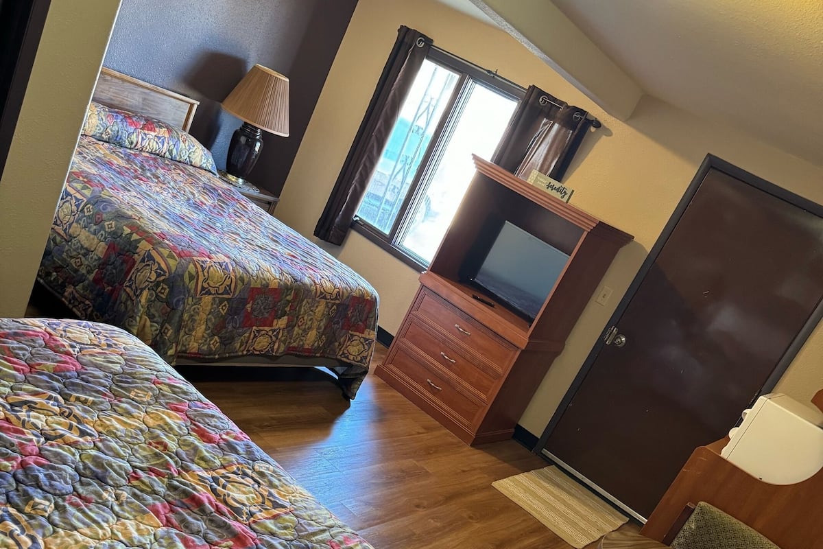 A hotel room with two beds, a TV, a desk, and a chair.