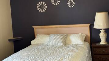 A neatly made bed with a textured white duvet, a wooden headboard, and a bedside table with a lamp.