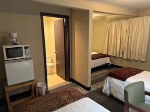A hotel room with a microwave on a small table, a bed with a patterned bedspread, a second bed with a plain bedspread, a bathroom with a toilet, and a shower curtain. - Rustic Lodge (Glasgow)