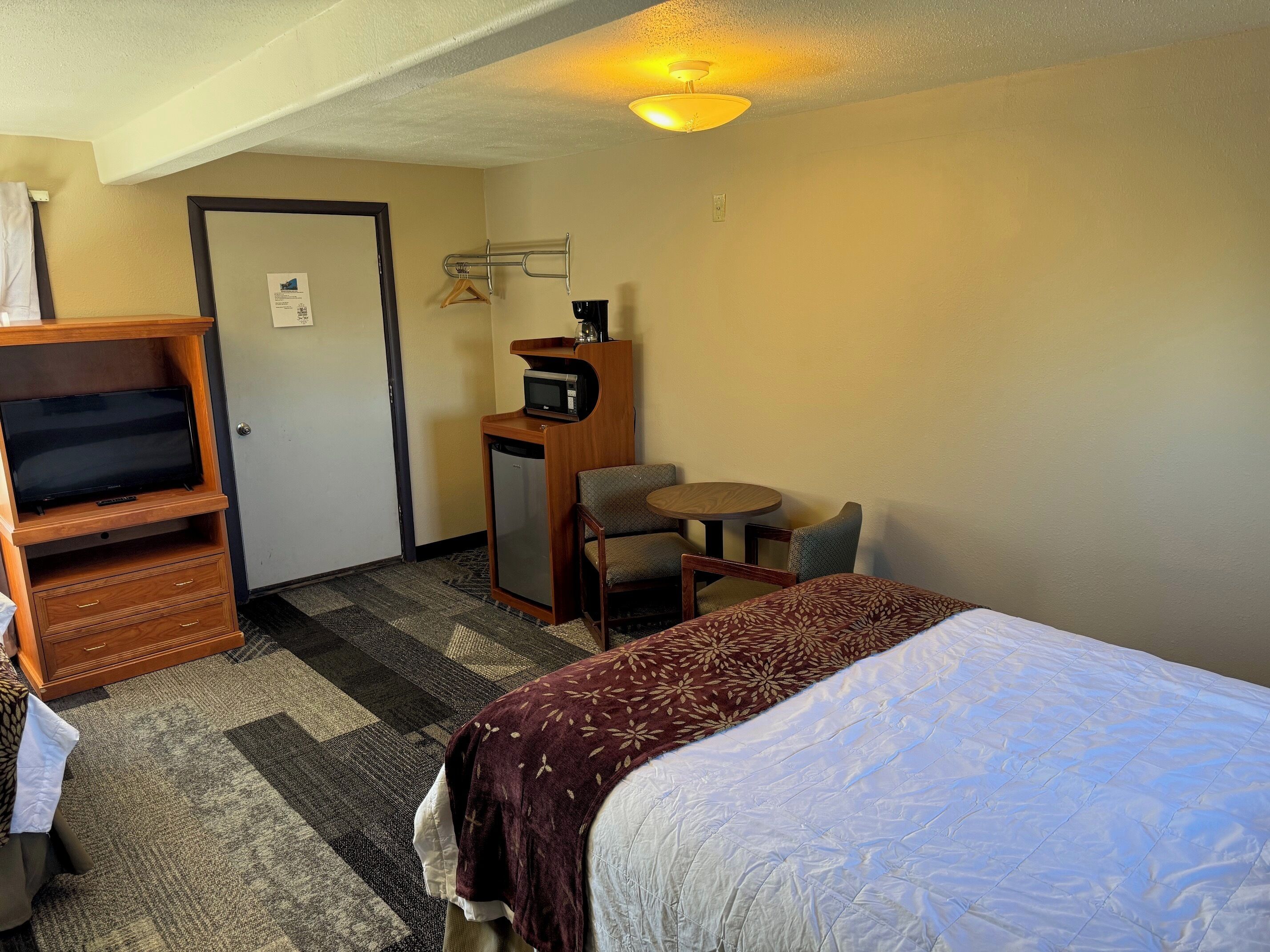 A hotel room with a bed, a desk with a computer, a chair, a TV, and a coat rack.