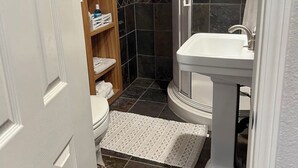 A bathroom with a white pedestal sink, a shower enclosure, a toilet, and a wooden shelf with toiletries. - Charming studio with WiFi, AC and a pool in fabulous Oakdale (Oakdale)