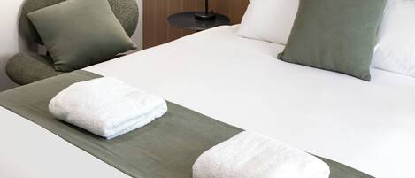 A hotel room with a neatly made bed, a green throw blanket, and a white towel.