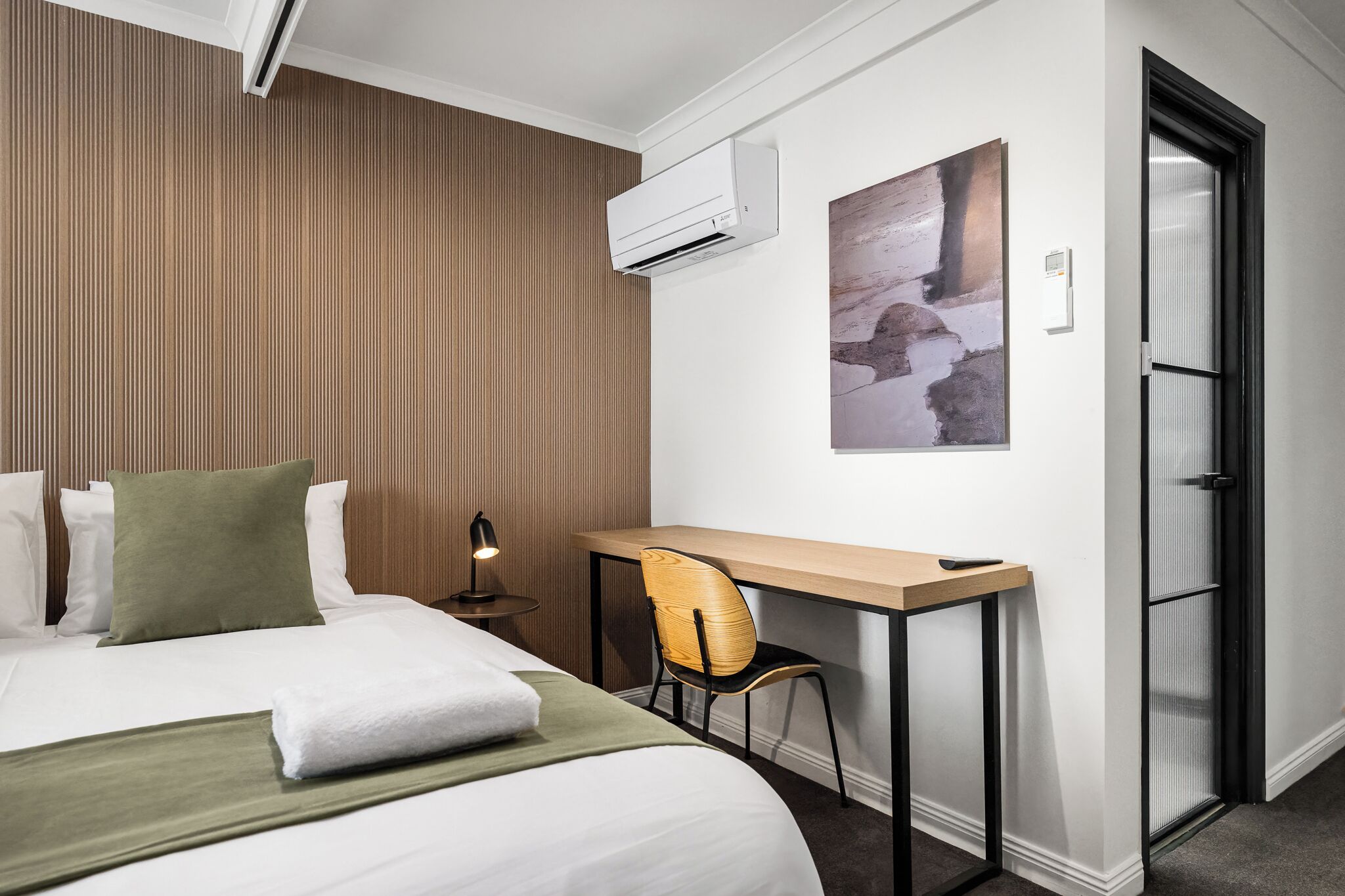 Habitación de hotel con cama, escritorio, silla, aire acondicionado y puerta.