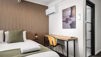 Habitación de hotel con cama, escritorio, silla, aire acondicionado y puerta.