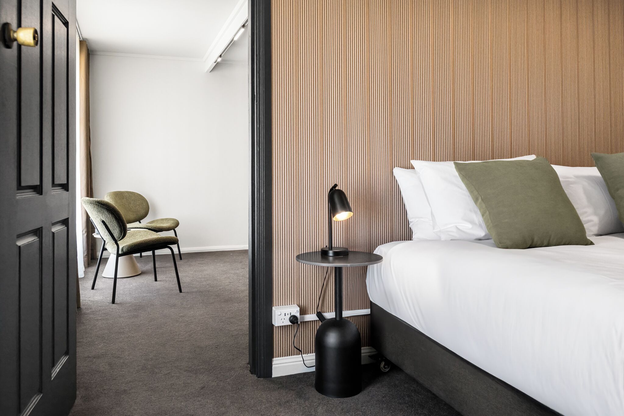Ein Hotelzimmer mit einem Bett, einem Sessel, einem Nachttisch mit Lampe und einer Wand mit vertikalen Linien.