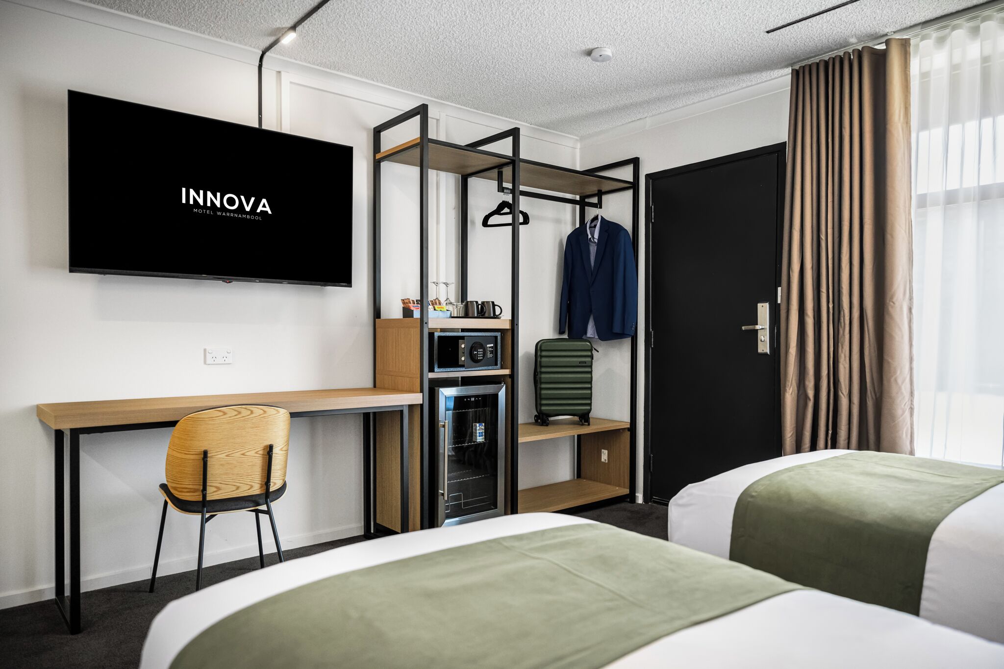 A hotel room with a bed, a desk, a TV, a wardrobe, and a minibar.