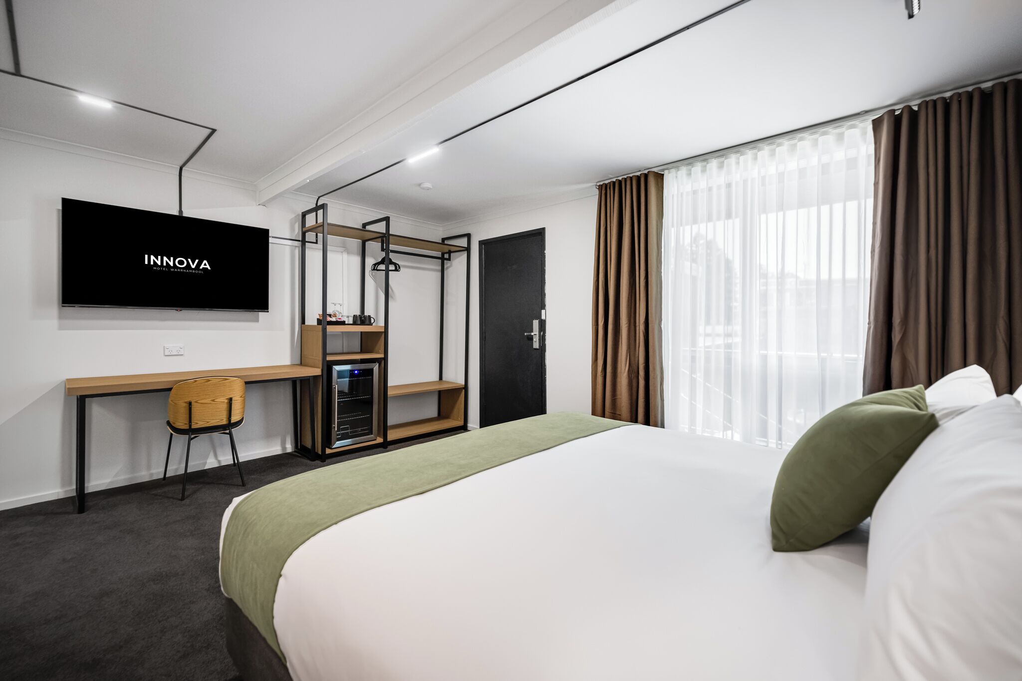 Hotellihuone, jossa on sänky, työpöytä tuolilla, televisio ja vaatekaappi.