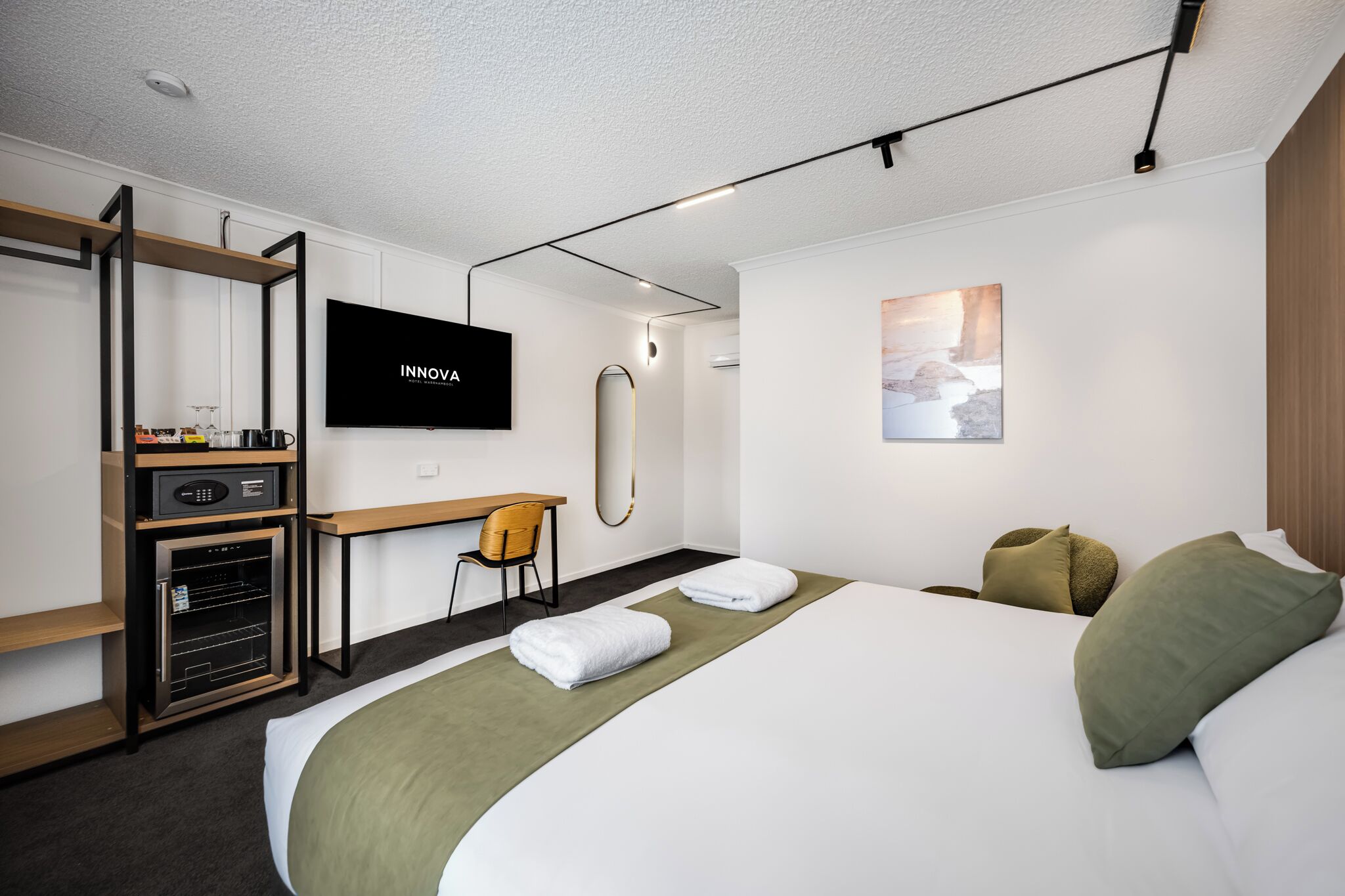 Quarto de hotel com uma cama, uma escrivaninha, uma televisão e um minibar.