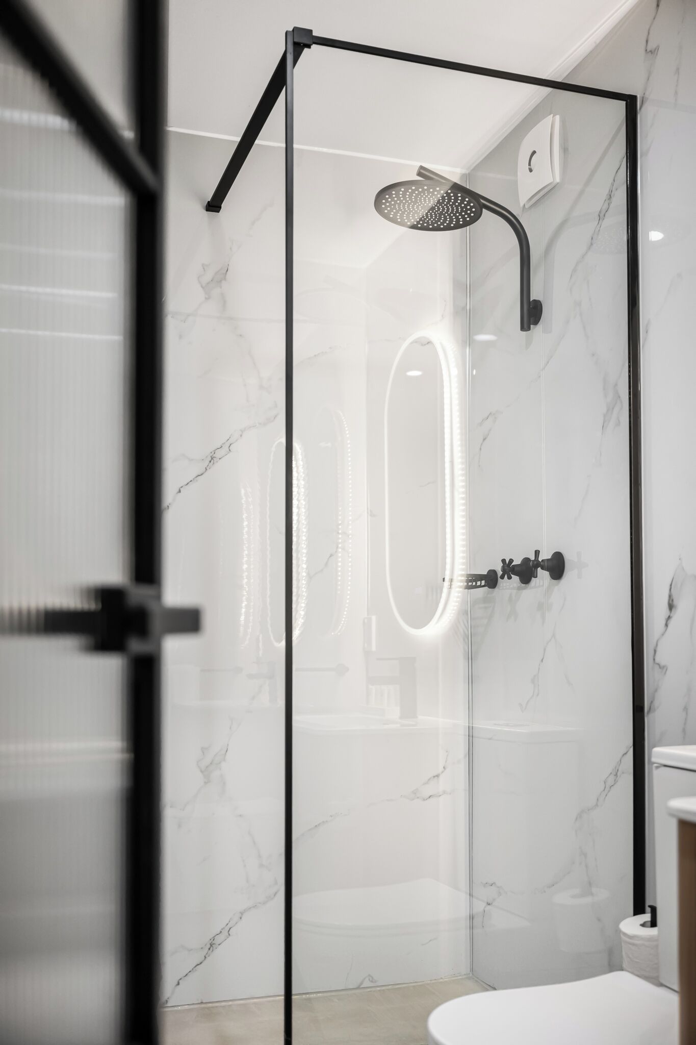 Un baño moderno con ducha de vidrio, paredes de mármol y un inodoro blanco.