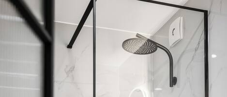 Un baño moderno con ducha de vidrio, paredes de mármol y un inodoro blanco.