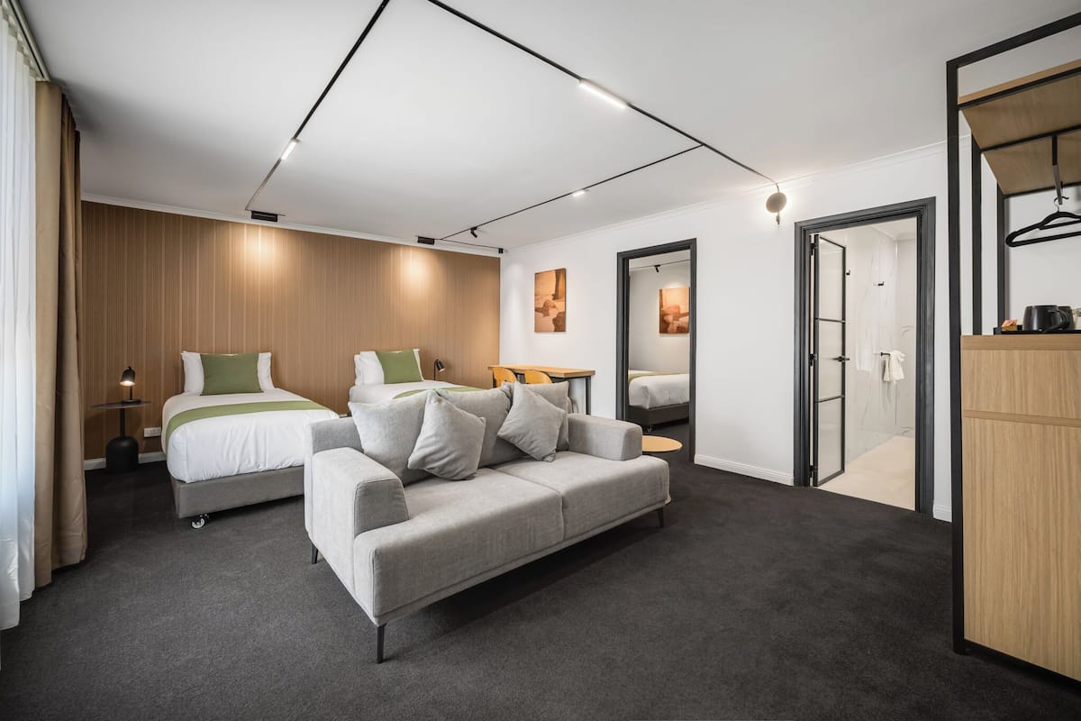 A modern hotel room with a large bed, a sofa, a desk, and a wardrobe.