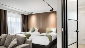 A modern hotel room with two beds, a sofa, and a glass partition.