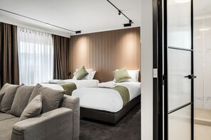 A modern hotel room with two beds, a sofa, and a glass partition.