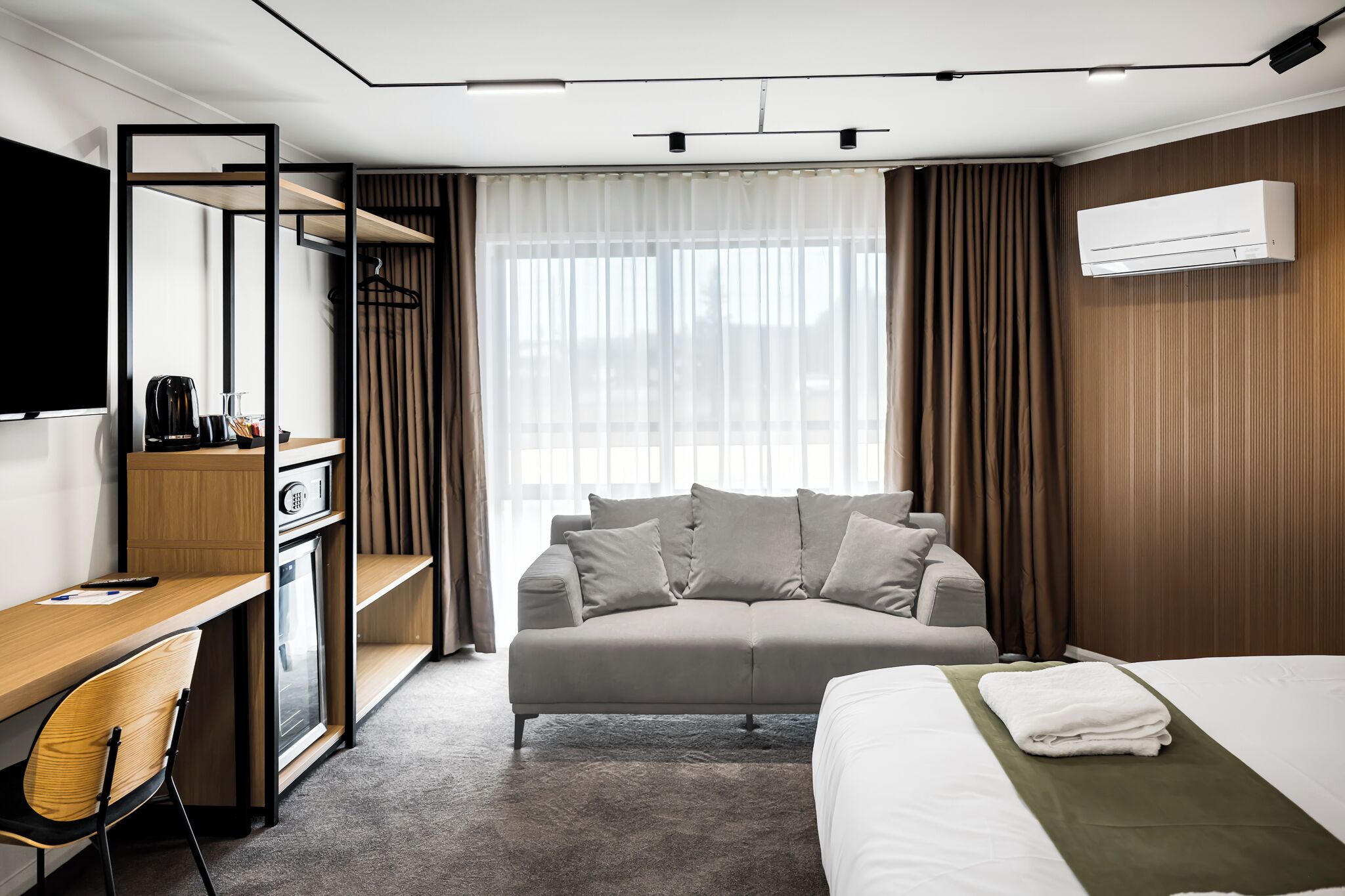 A modern hotel room with a bed, a sofa, a desk, and a TV.