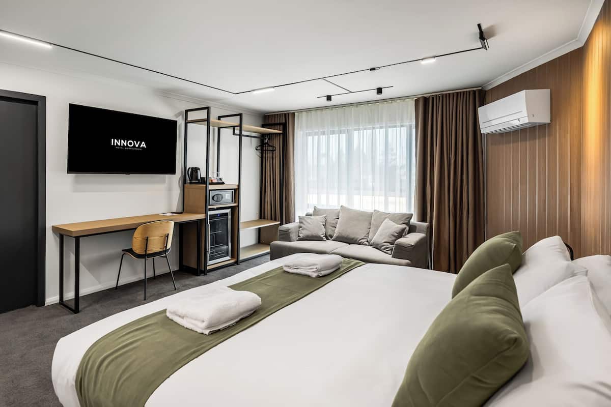 A modern hotel room with a bed, a desk, a chair, a TV, and a coffee machine.