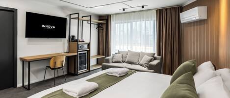 A modern hotel room with a bed, a desk, a chair, a TV, and a window with curtains.